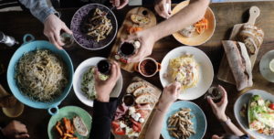 variety of italian food on wooden table and three people clinking their wine glasses